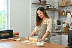 微笑家庭主妇穿围裙销滚动面团厨房表格使面包现代厨房