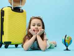 特写镜头可爱的旅行者孩子女孩全球黄色的手提箱孤立的蓝色的颜色背景