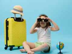 好奇的旅行者女孩相机古董双筒望远镜黄色的手提箱蓝色的颜色背景