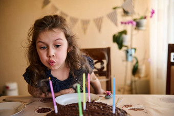 可爱的快乐孩子长卷曲的头发生日女孩优雅的海军衣服吹蜡烛生日蛋糕