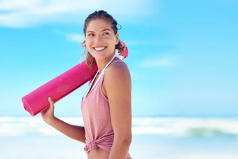 海边瑜伽年轻的女人持有瑜伽席站海滩