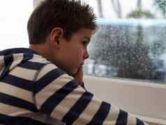 多雨的天年轻的男孩坐着窗口无聊降雨
