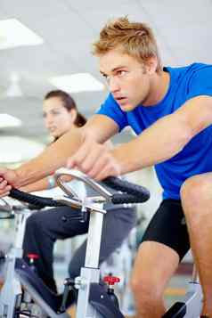 身体有意识的年轻的男人。锻炼旋转自行车健身房