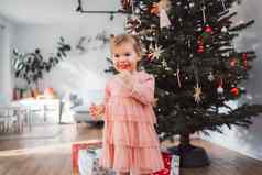 快乐的女孩红色的棒棒糖站前面圣诞节树美丽的粉红色的衣服