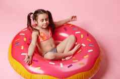 可爱的孩子女孩冥想莲花位置粉红色的充气游泳环甜甜圈粉红色的颜色背景