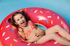 前视图迷人的孩子女孩椰子喝放松浮动甜甜圈游泳环孤立的蓝色的背景