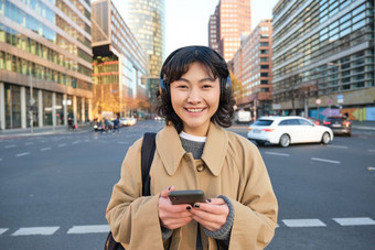肖像年轻的亚洲女孩学生走城市听音乐耳机移动电话街道