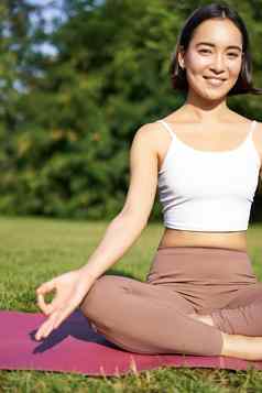 垂直拍摄年轻的亚洲女人坐着健身席冥想平静的放松练习公园显示Zen标志