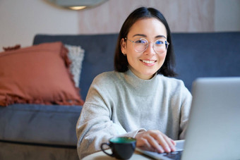 自由职业者年轻的微笑女人自由职业者住首页工作远程移动PC穿眼镜坐着生活房间