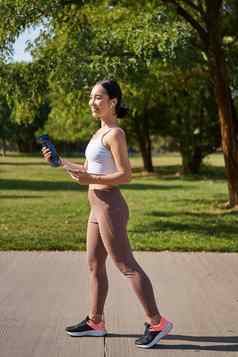 活跃的亚洲女孩健身服装锻炼公园走运动服装智能手机水瓶