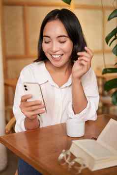 肖像现代女孩坐在咖啡咖啡馆微笑智能手机阅读书餐厅移动电话应用程序