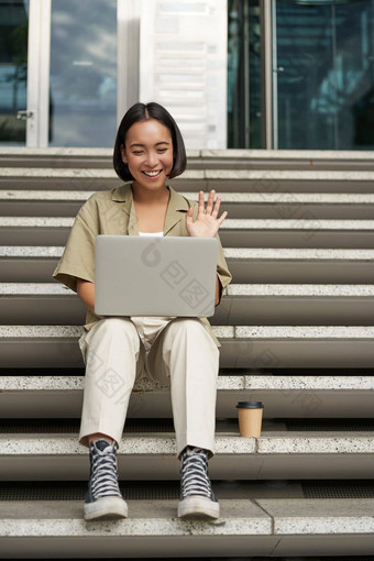 肖像年轻的亚洲女孩学生会谈移动PC视频闲谈，聊天说话在线会议坐着在户外楼梯