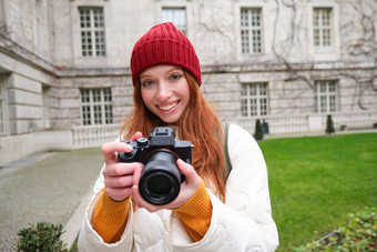 红色头发的人女孩摄影师需要照片专业相机在户外捕捉streetstyle照片兴奋采取图片