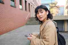 时尚的现代亚洲女孩学生无线耳机走城市背包微笑快乐脸