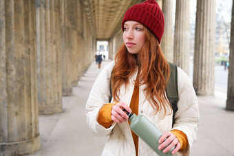 年轻的红色头发的人女孩持有热水瓶手倒热喝走城市旅游需要打破打开瓶点心饮料