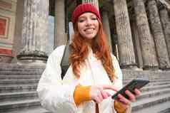 肖像年轻的城市女孩背包智能手机走城市地图移动应用程序检查方向
