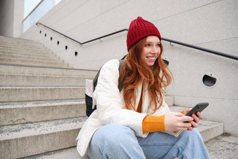 时尚的欧洲女孩<strong>红色</strong>的头发坐在公共楼梯智能手机的地方在线订单发<strong>送</strong>消息移动电话社会应用程序微笑幸<strong>福</strong>的