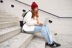 微笑红色头发的人女孩学生坐在楼梯在户外移动PC连接公共无线网络城市作品项目互联网电脑