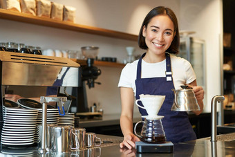 微笑女孩咖啡师亚洲酒保<strong>倒水水壶</strong>酝酿过滤器咖啡咖啡馆计数器穿蓝色的围裙
