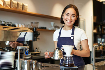 微笑女孩咖啡师亚洲酒保<strong>倒水水壶</strong>酝酿过滤器咖啡咖啡馆计数器穿蓝色的围裙
