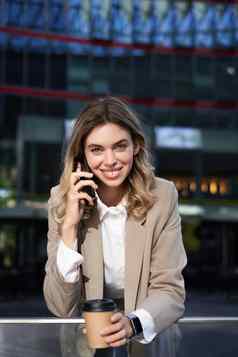垂直拍摄微笑女商人回答移动电话调用会说话的智能手机喝咖啡