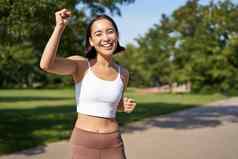 快乐健身女孩实现目标完成马拉松运行手庆祝胜利慢跑并公园