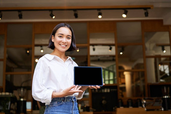 微笑亚洲女人显示数字平板电脑屏幕咖啡馆老板显示smth<strong>站前</strong>面咖啡馆入口