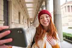 可爱的年轻的红色头发的人女人需要自拍街移动电话使照片智能手机应用程序街