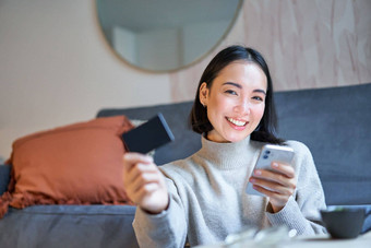 微笑亚洲女孩智能手机信贷卡购物在线移动电话订单首页交付