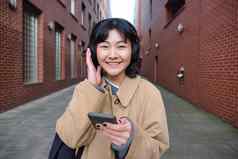 美丽的微笑女人走小镇听音乐移动电话应用程序大学穿耳机