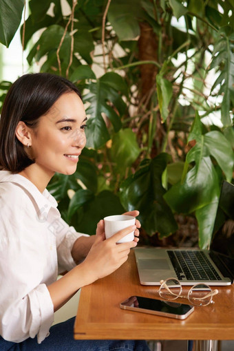 垂直拍摄美丽的女人坐在咖啡馆移动PC作品研究在线联合办公空间微笑放松