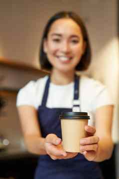 微笑亚洲咖啡师女孩给外卖咖啡杯准备外卖订单客人咖啡馆穿围裙统一的