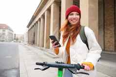 红色头发的人女孩旅游背包移动电话租金e-scooter街道欧洲城市