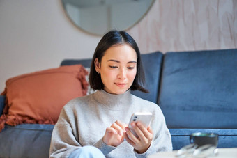 肖像微笑亚洲女人坐在首页智能手机应用程序订单交付消息移动电话应用程序