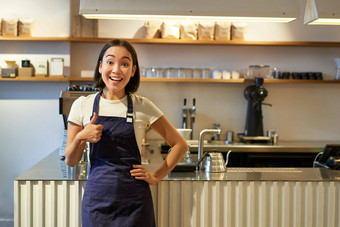 微笑<strong>女孩</strong>学生工作兼职咖啡馆咖啡师显示拇指穿<strong>围裙</strong>站咖啡商店计数器