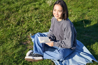肖像亚洲女孩阅读书坐着毯子公园绿色草微笑幸福的