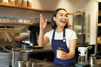 肖像微笑亚洲女孩咖啡师给订单咖啡馆邀请客人选择<strong>外卖</strong>订单计数器持有<strong>外卖</strong>杯咖啡