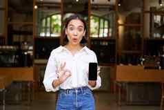 热情的年轻的亚洲女孩女服务员咖啡馆显示移动电话应用程序指出智能手机屏幕