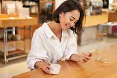 肖像美丽的亚洲女人智能手机放松咖啡馆坐着享受咖啡移动电话