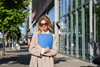 肖像企业女人太阳镜米色西装持有蓝色的文件夹办公室文档工作走街阳光明媚的一天