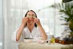 年轻的女人浴袍黄瓜片眼睛采取水疗中心护肤品程序美治疗排毒概念