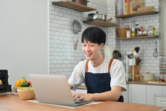 微笑年轻的亚洲男人。自由职业者移动PC工作远程工作首页坐着舒适的厨房室内
