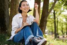 肖像年轻的亚洲女人写作笔记本表达的想法纸日记微笑坐着树夏天一天公园