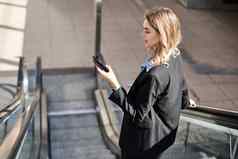 肖像女人自动扶梯移动电话智能手机屏幕站黑色的西装街