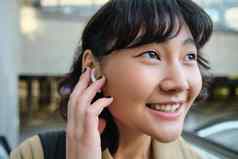 关闭肖像微笑朝鲜文女孩耳机听音乐无线耳机享受旅行小镇最喜欢的歌曲播放列表