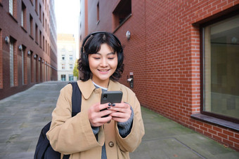 肖像年轻的朝鲜文女人走城市背包耳机听<strong>音</strong>乐智能手机电话应用程序<strong>街道</strong>