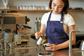 快乐微笑咖啡馆老板女孩咖啡师围裙使卡布奇诺咖啡拿铁艺术蒸牛奶站计数器