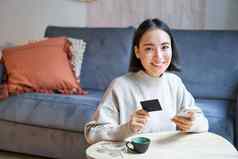 微笑可爱的亚洲女人信贷卡智能手机支付账单在线持有移动电话相机