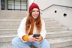 红色头发的人女孩红色的他坐在楼梯移动电话现代女人持有智能手机发短信消息电话应用程序在户外