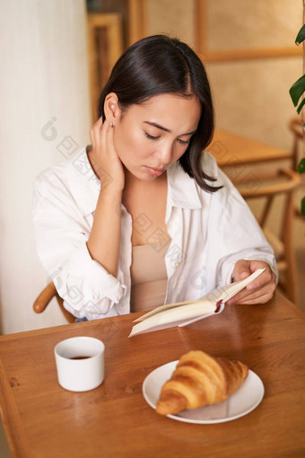 亚洲女孩阅读书伤心坐着咖啡馆喝咖啡深思熟虑的生闷气的脸